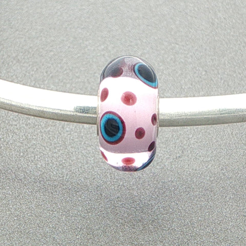 Polka dot murano glass bead with a pink core and burgundy dots with some with blue and black centres on a silver bangle against a grey background