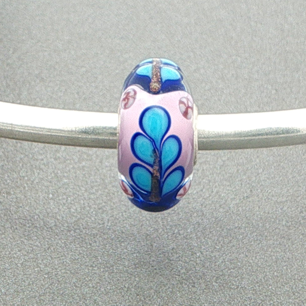 Decorative murano glass bead with blue and pink patterns on a silver bangle against a grey background