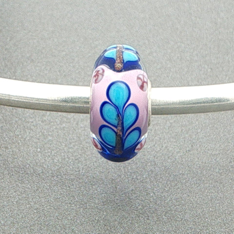 Decorative murano glass bead with blue and pink patterns on a silver bangle against a grey background