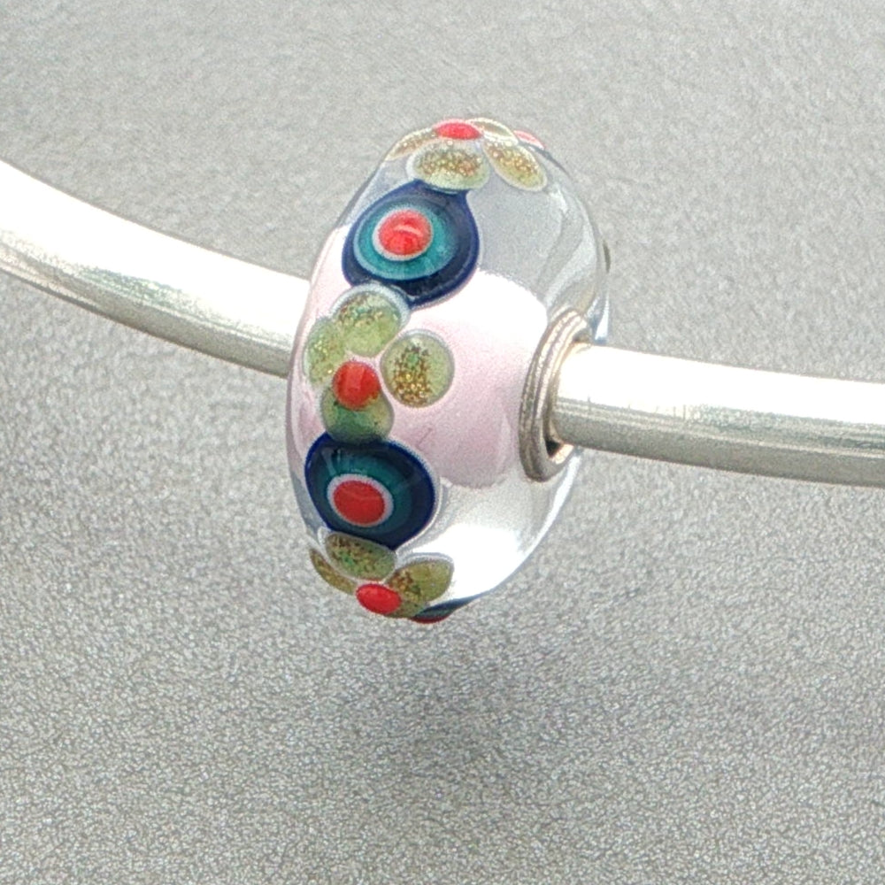 Glass bead with colourful floral and circular patterns on a silver bangle against a grey background