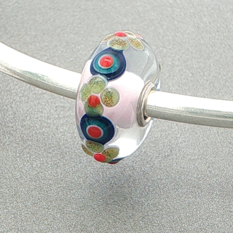 Glass bead with colourful floral and circular patterns on a silver bangle against a grey background