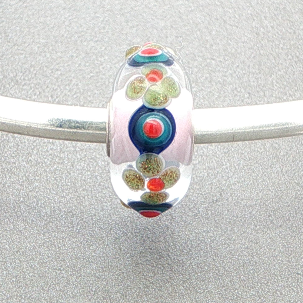 Colorful glass bead with floral and dot pattern on a silver bangle against a grey background