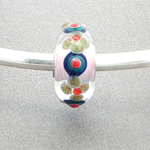 Colorful glass bead with floral and dot pattern on a silver bangle against a grey background