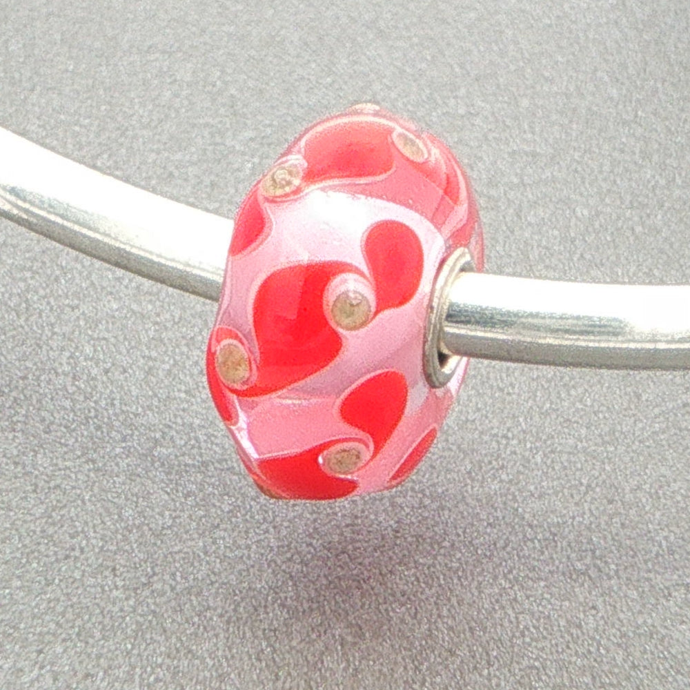 Glass bead with red and gold pattern design on a silver bangle against a grey background