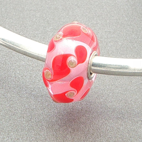 Glass bead with red and gold pattern design on a silver bangle against a grey background