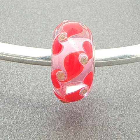Red and gold glitter patterned murano glass bead with a pale pink core on a silver bangle against a grey background
