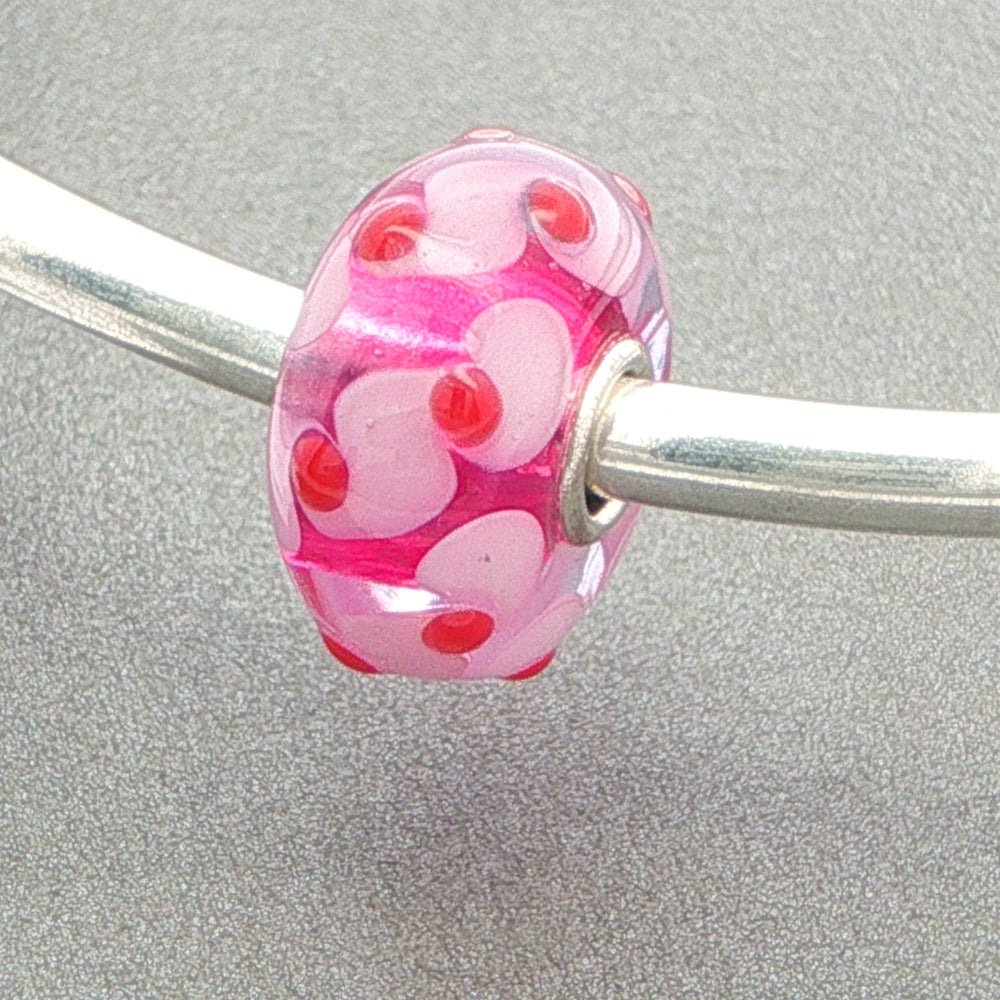 Pink glass bead with red dots and pink details on a silver bangle against a grey background