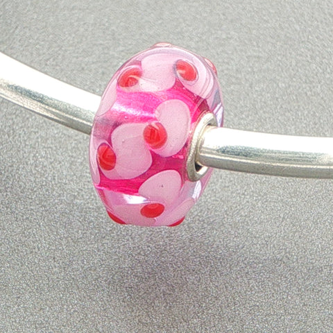 Pink glass bead with red dots and pink details on a silver bangle against a grey background