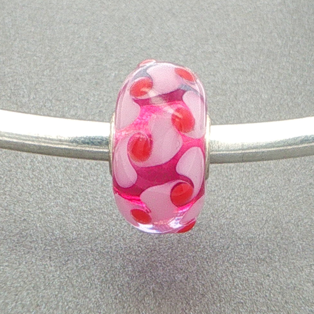 Murano glass bead with a pale pink and red design with a vibrant pink core on a silver bangle against a grey background