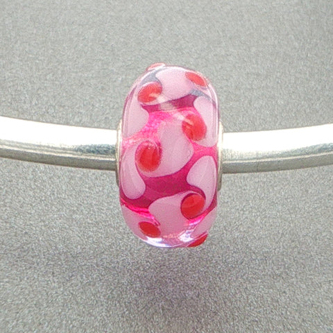 Murano glass bead with a pale pink and red design with a vibrant pink core on a silver bangle against a grey background