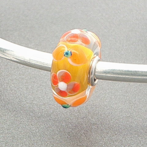 Glass bead with a summer floral design on a silver bangle against a grey background