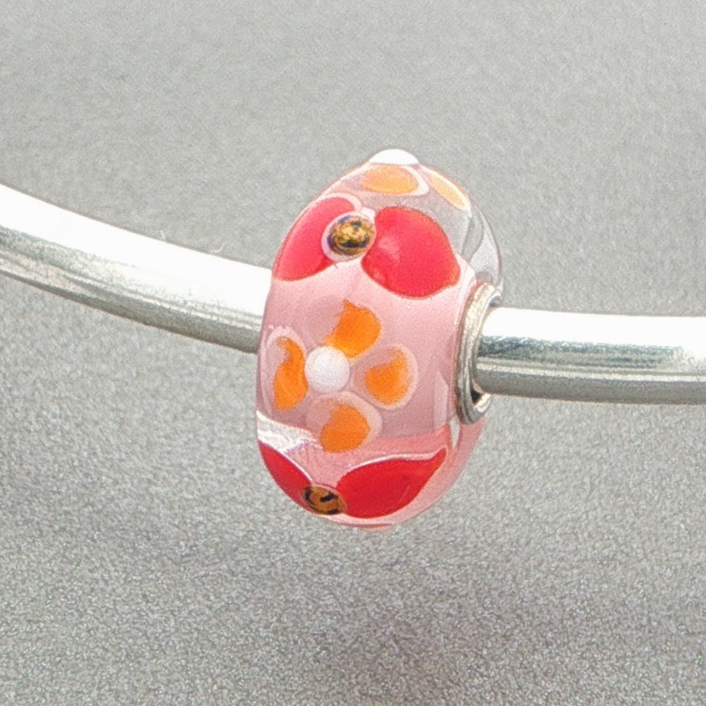 Glass bead with floral pattern on a silver bangle against a grey background
