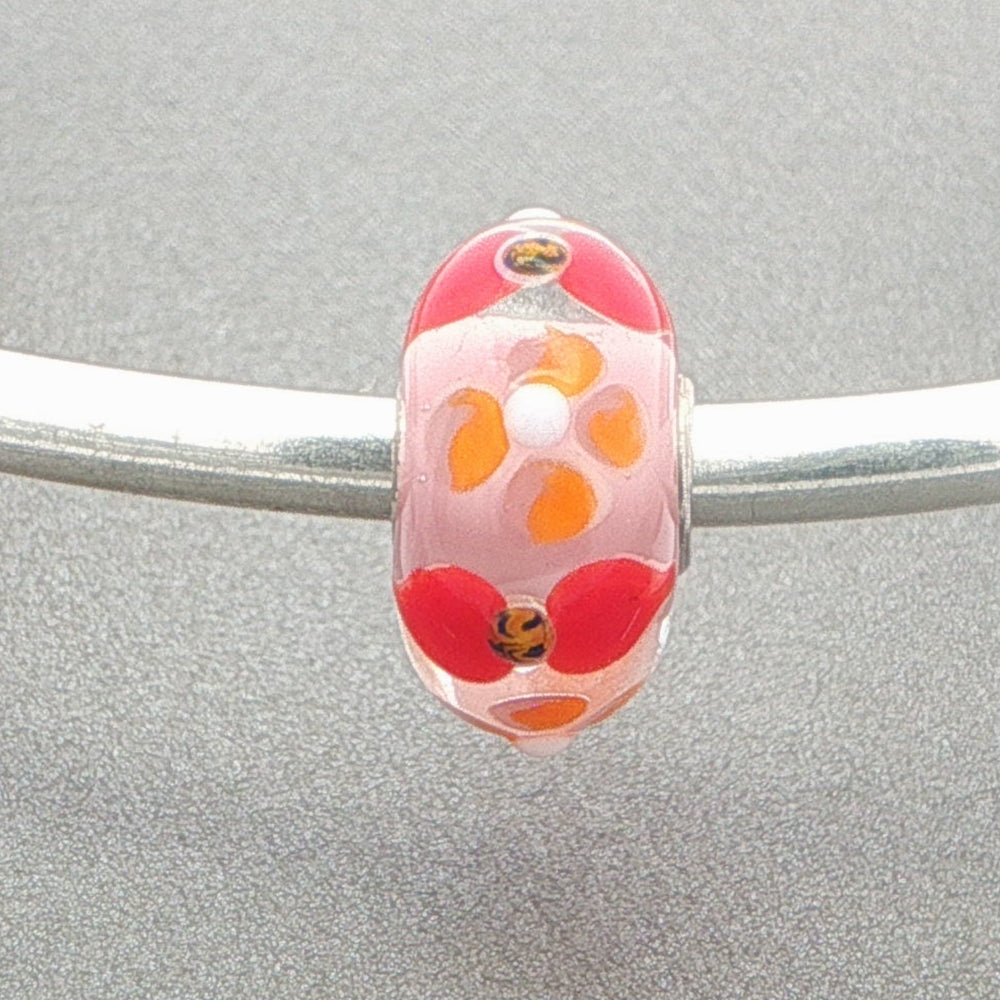 Glass bead with a floral design on a silver bangle against a grey background