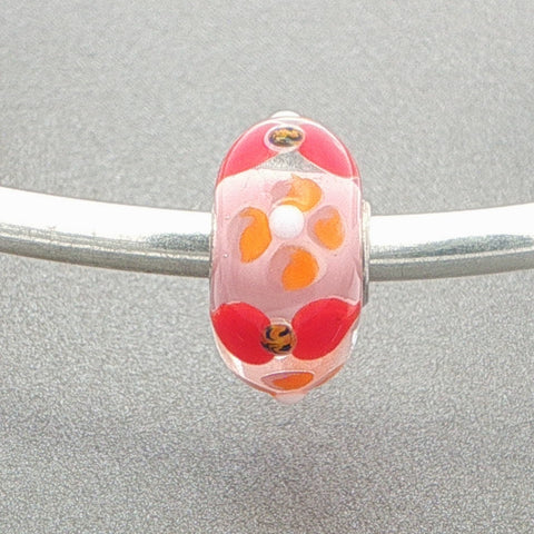 Glass bead with a floral design on a silver bangle against a grey background
