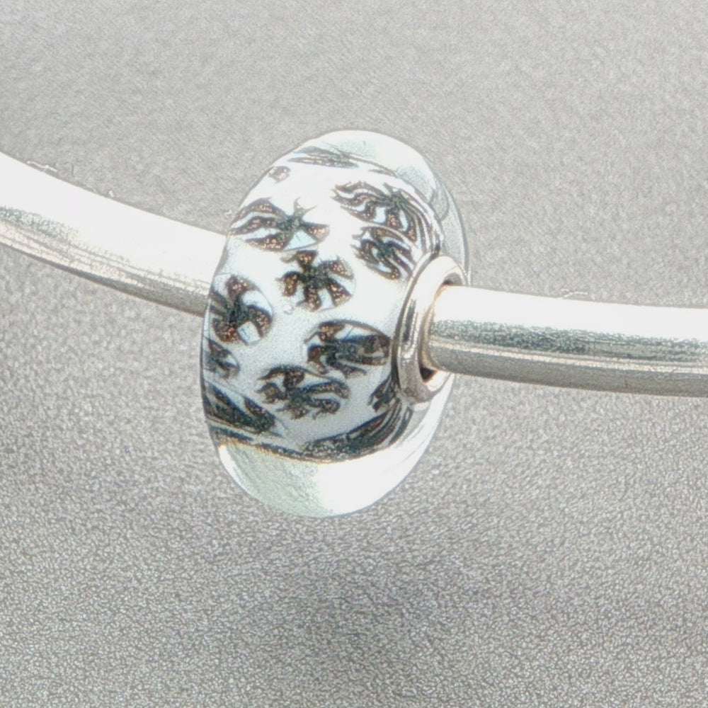Glass bead with a glitter fan-like pattern and white core on a silver bangle against a grey background
