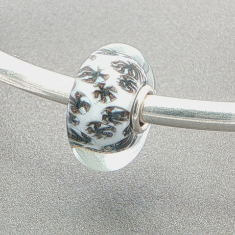 Glass bead with a glitter fan-like pattern and white core on a silver bangle against a grey background
