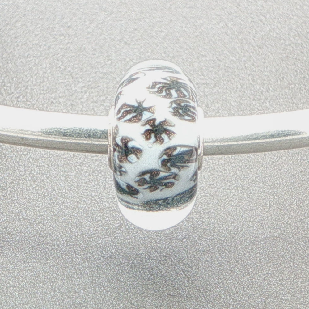 Murano glass bead with white core and glitter fan-like design on a silver bangle against a grey background