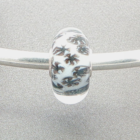 Murano glass bead with white core and glitter fan-like design on a silver bangle against a grey background