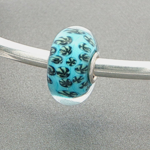 Glass bead with a coral-like pattern and blue core on a silver bangle against a grey background