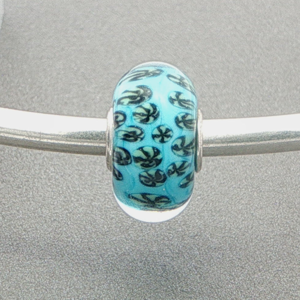 Murano glass bead with blue core and fan-like design on a silver bangle against a grey background