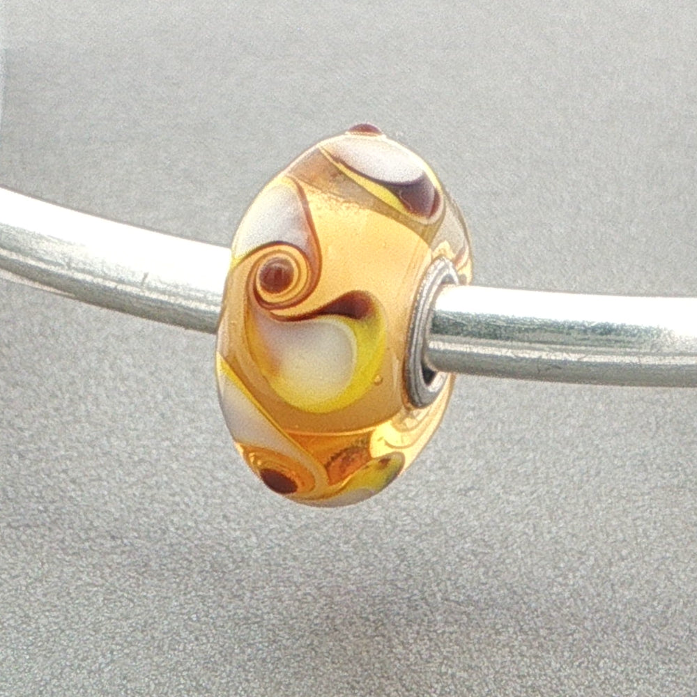 Glass bead with spinner pattern on a silver bangle against a grey background