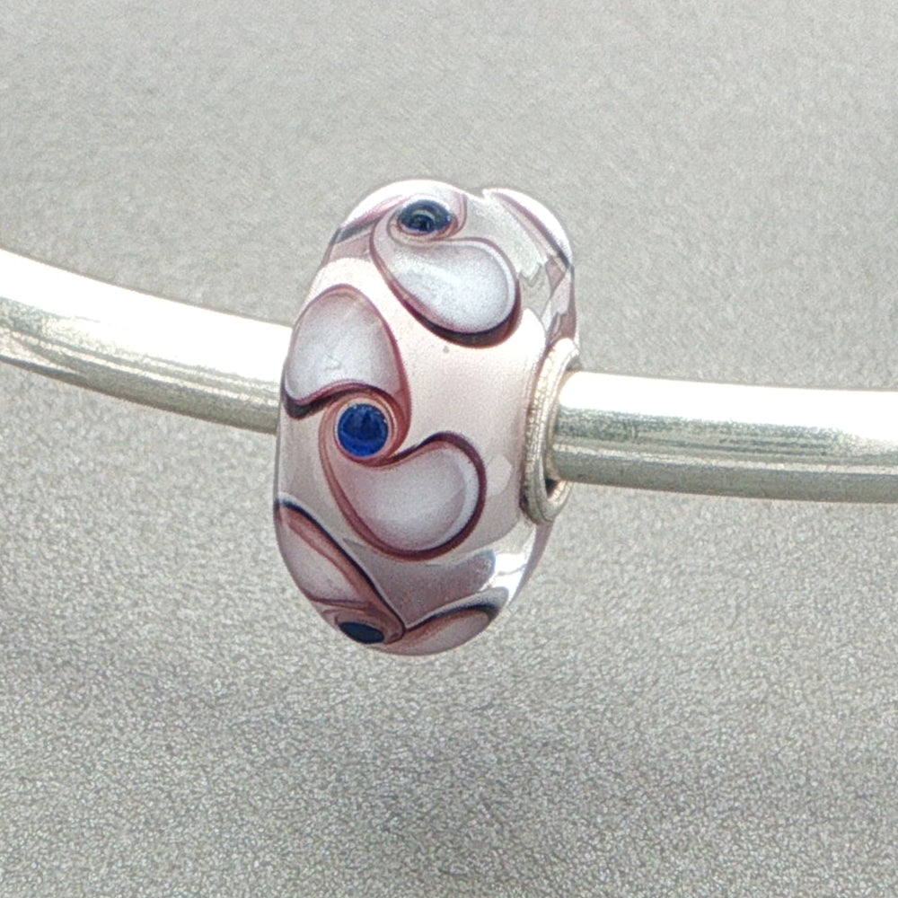 Decorative glass bead with spinner pattern on a silver bangle against a grey background
