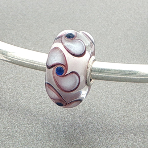 Decorative glass bead with spinner pattern on a silver bangle against a grey background