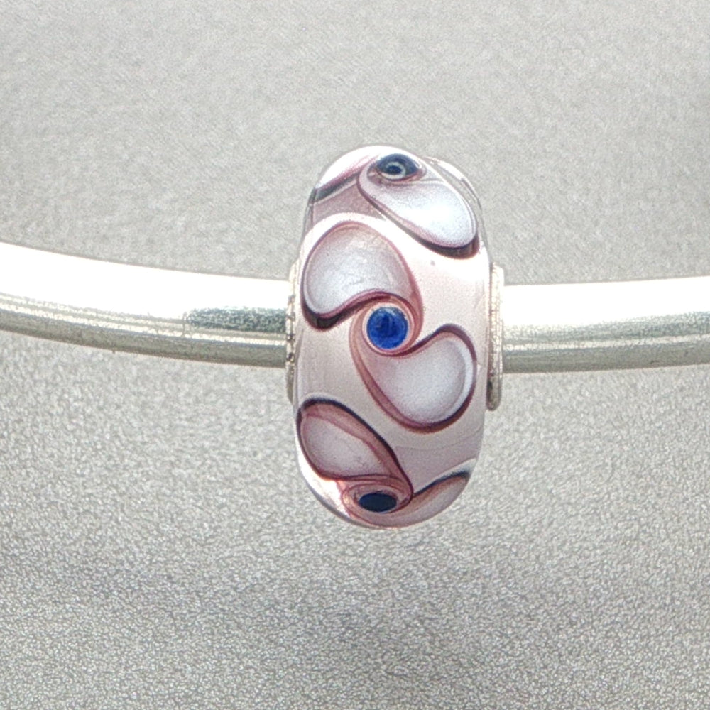 Murano glass bead with white core and spinner pattern on a silver bangle against a grey background