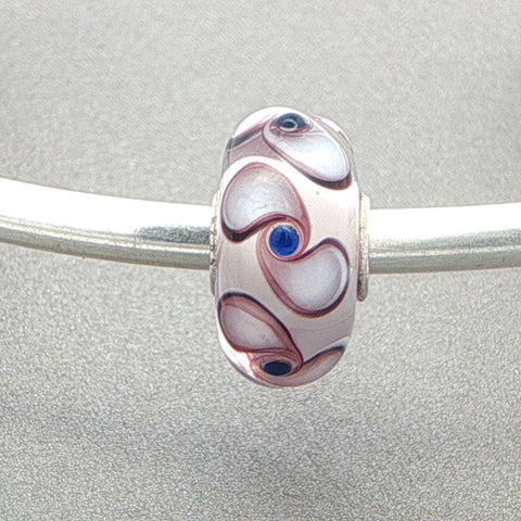 Murano glass bead with white core and spinner pattern on a silver bangle against a grey background