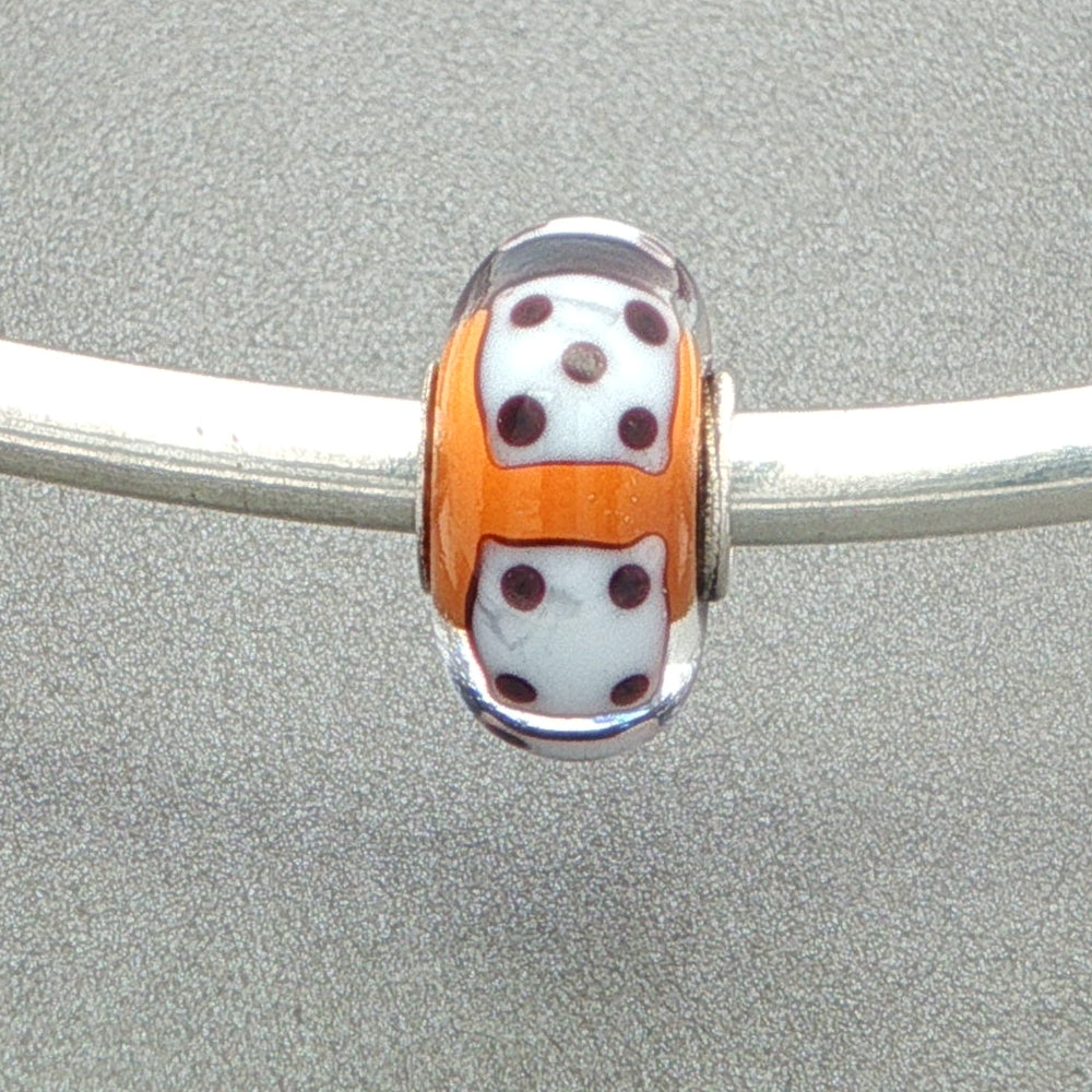 Murano glass bead with orange core and white dice design on a silver bangle against a grey background