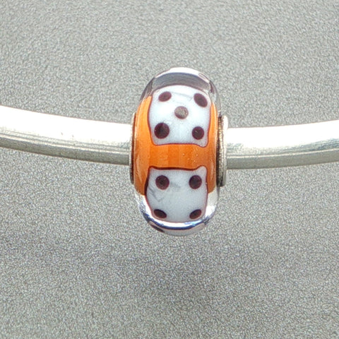 Murano glass bead with orange core and white dice design on a silver bangle against a grey background