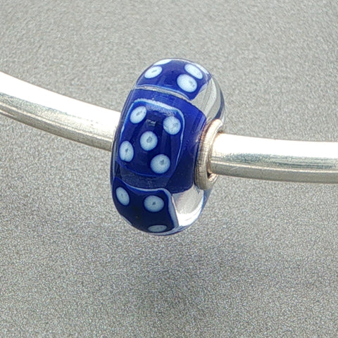 Glass bead with blue dice design and blue core on a silver bangle against a grey background