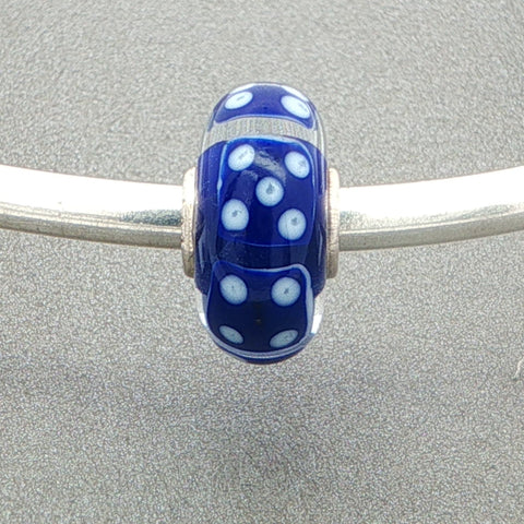 Murano glass bead with blue core and blue dice design on a silver bangle against a grey background