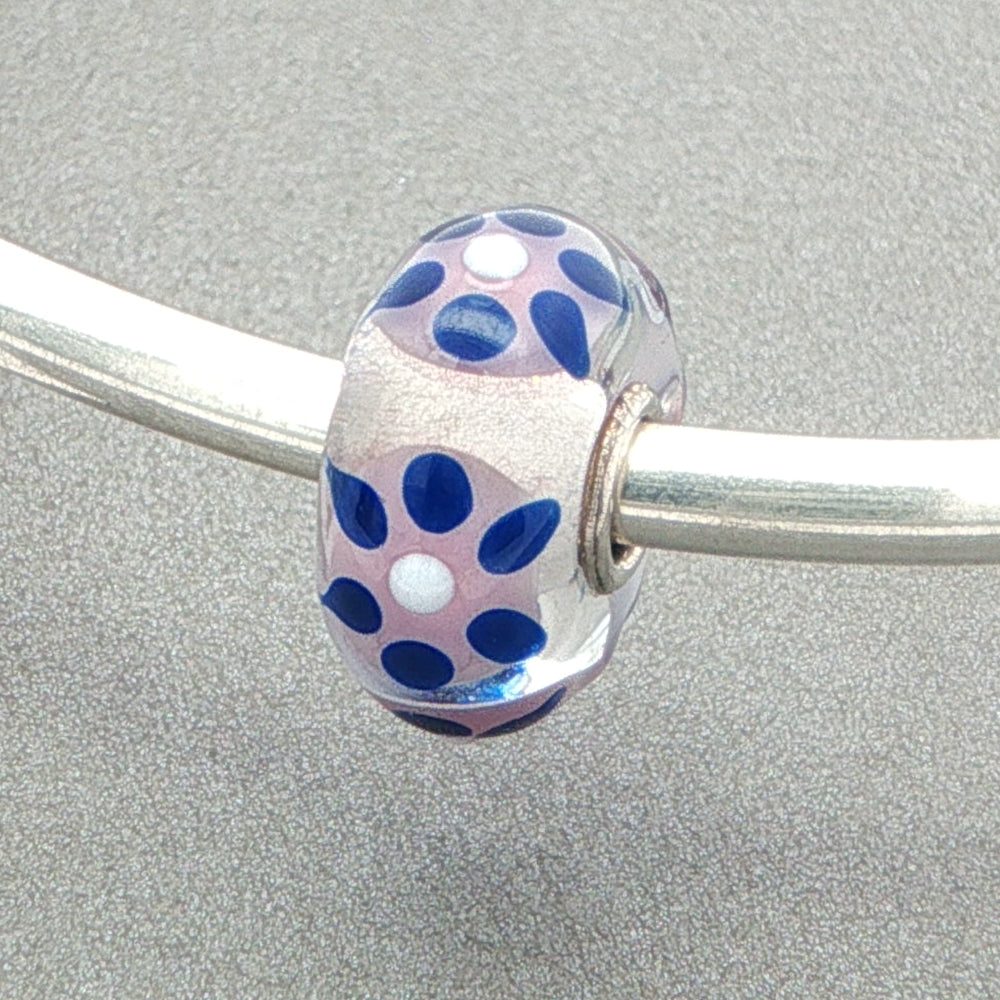 Glass bead with blue, white and pink pattern on a silver bangle against a grey background