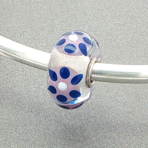 Glass bead with blue, white and pink pattern on a silver bangle against a grey background