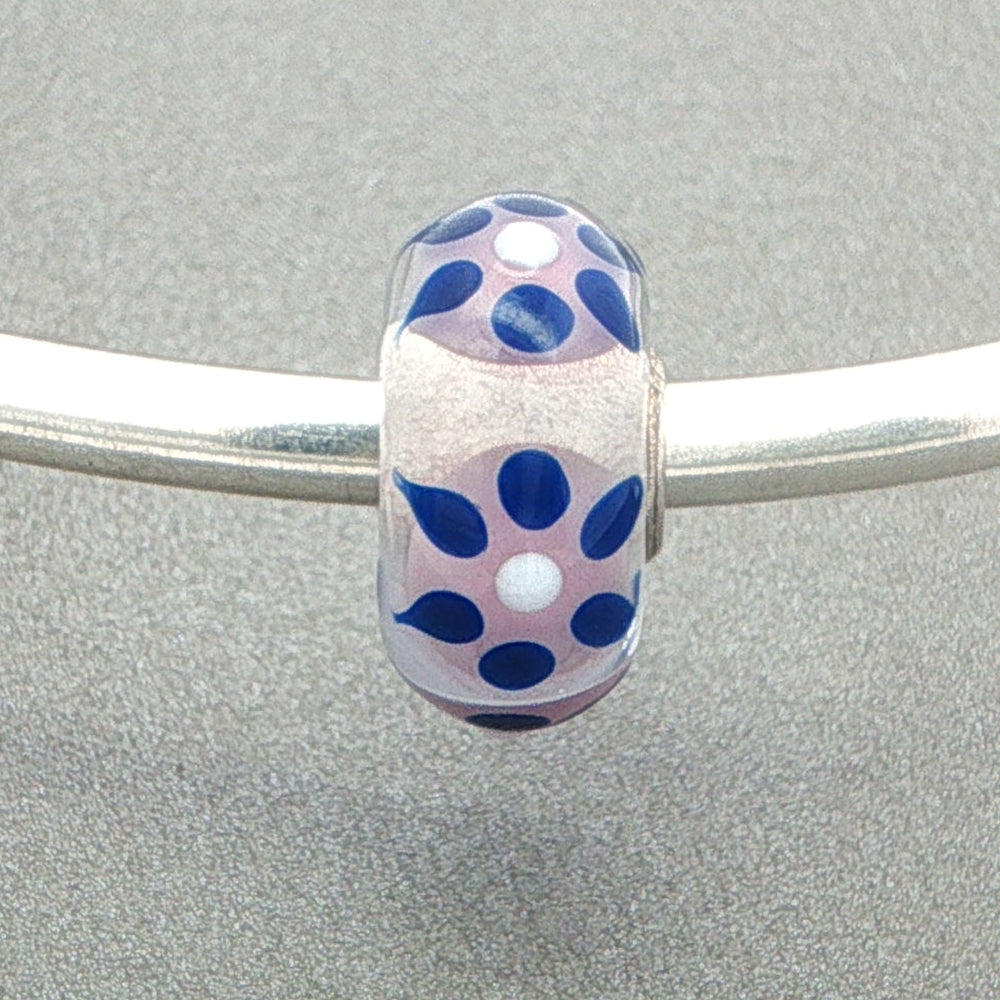Decorative glass bead with blue sun rays type design on a silver bangle against a grey background