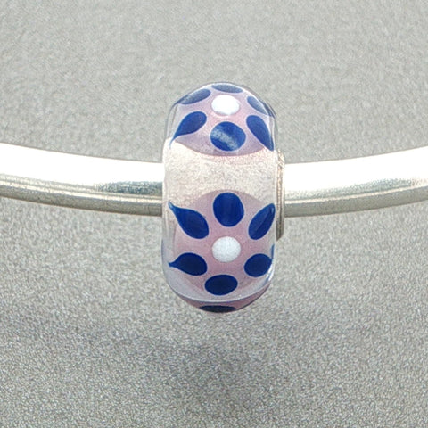 Decorative glass bead with blue sun rays type design on a silver bangle against a grey background