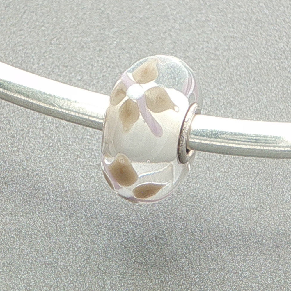 Glass bead with floral design on a silver bangle against a grey background