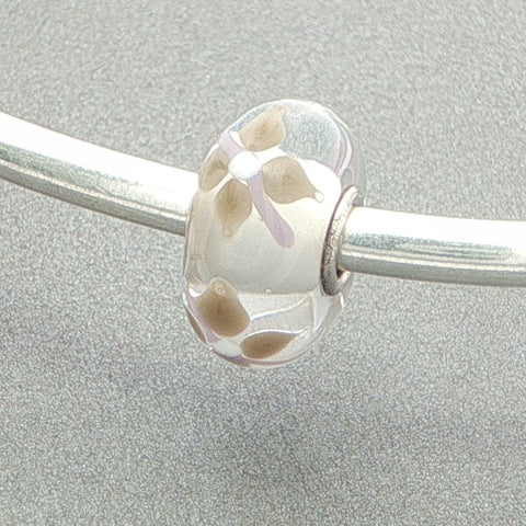 Glass bead with floral design on a silver bangle against a grey background