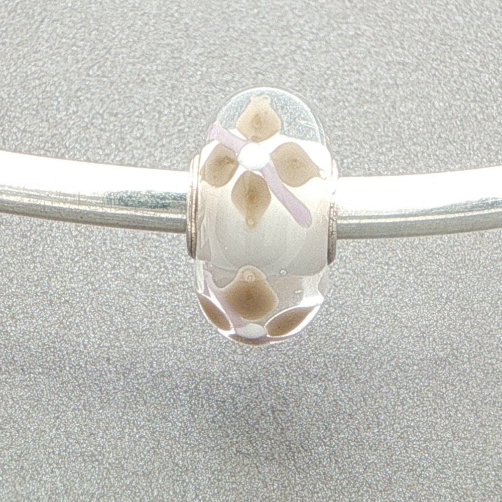 Murano glass bead with a white core and floral design on a silver bangle against a grey background
