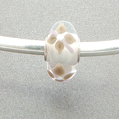 Murano glass bead with a white core and floral design on a silver bangle against a grey background